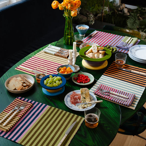 Dining table set with plates, glasses, and colorful placemats in a home setting.